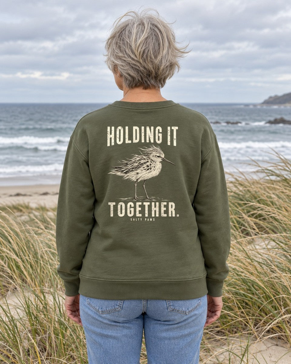 Holding It Together Sandpiper Back Design Midweight Sweatshirt in Military Green, worn by a model on a windy beach, back design