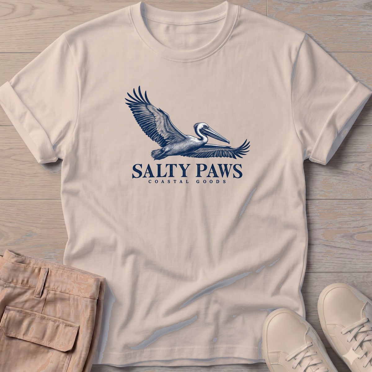 Gliding Pelican Coastal Goods T-Shirt in Sand, Salty Paws T-Shirt, front design flat lay