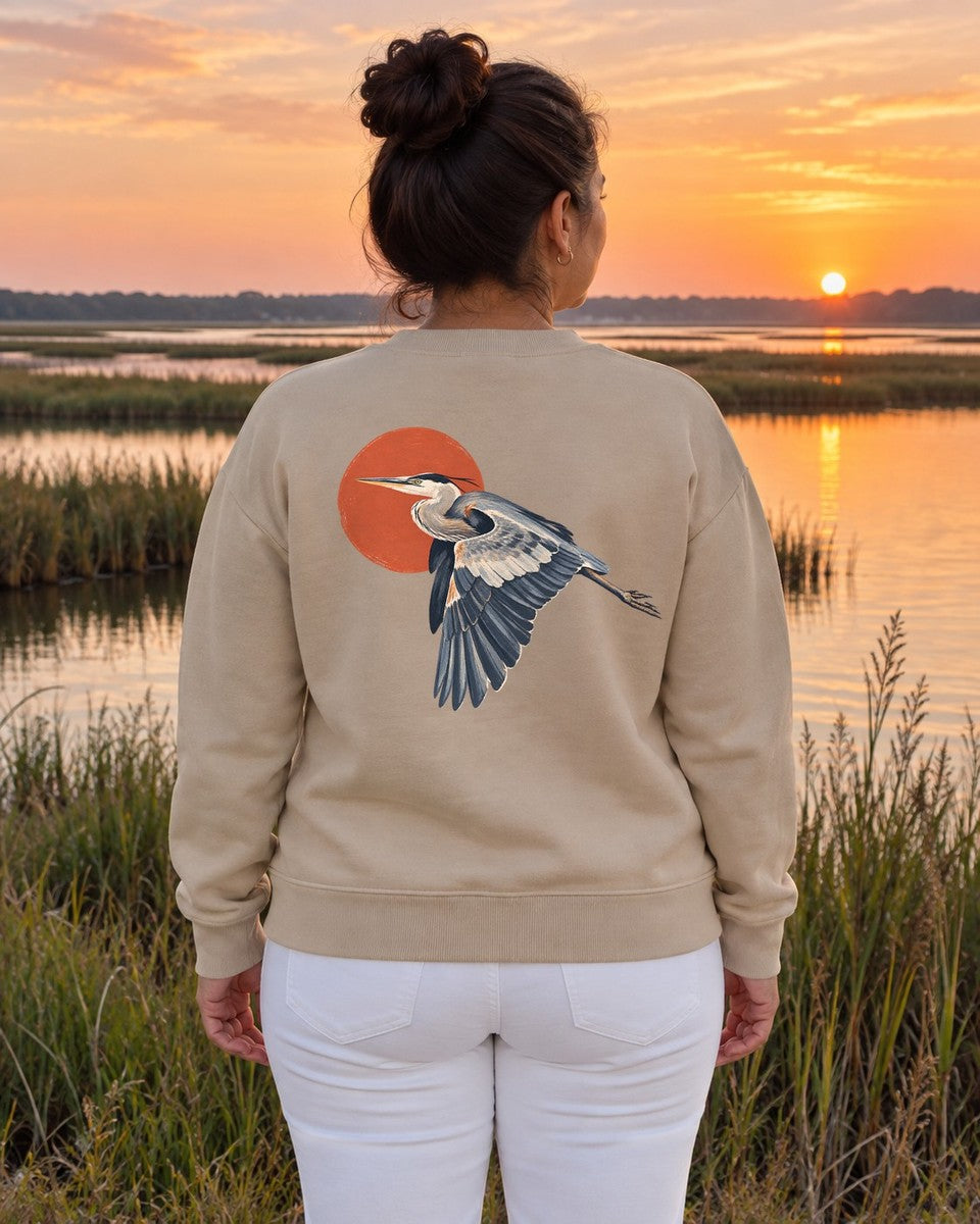 Great Blue Heron Red Sun Back Design Midweight Sweatshirt in Sand, worn by a model at a marsh at sunrise, back design