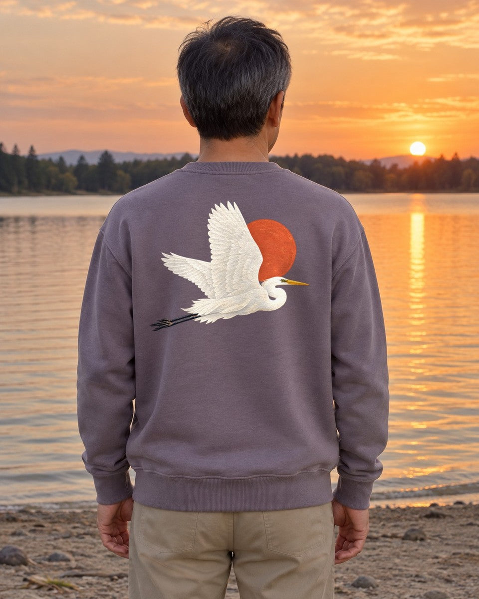 Great Egret Red Sun Back Design Midweight Sweatshirt in Paragon, worn by a model on a lake shore at sunset, back design